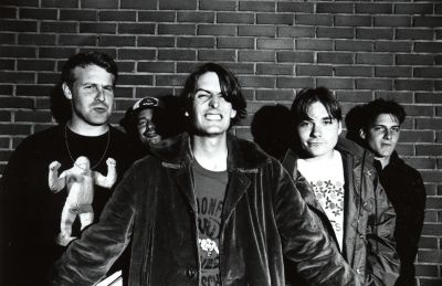 All 5 Pavement members posing for a band phoro in front of a brick wall.